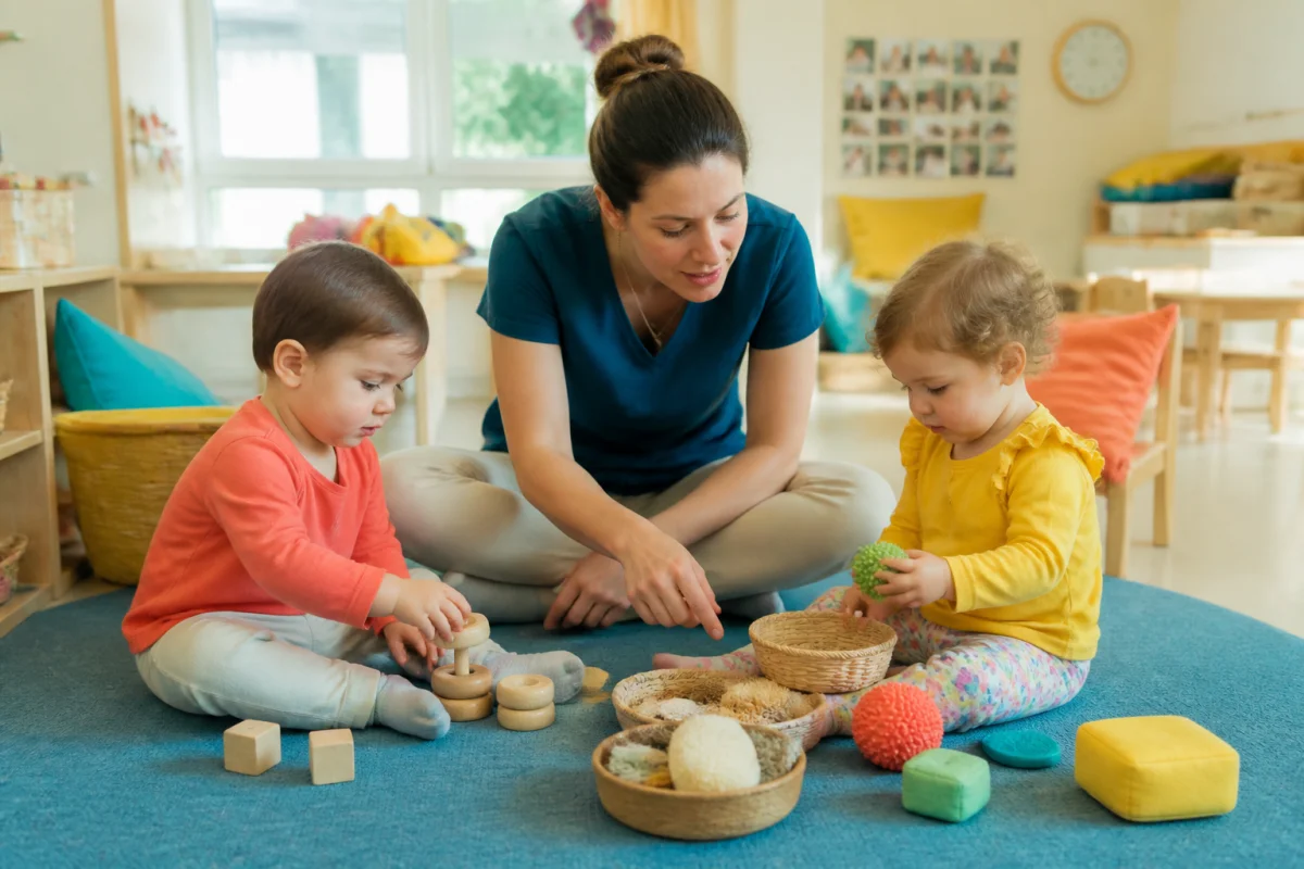 Éducatrice de jeunes enfants accompagnant deux tout-petits lors d’une activité sensorielle en crèche lumineuse